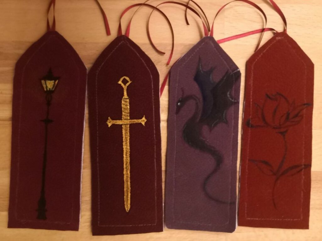 Vier Lesezeichen in Rottönen und darauf eine Laterne, ein Schwert, ein Drache und eine Rose gemalt